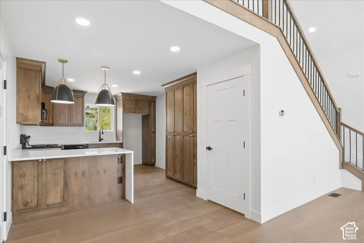 Kitchen featuring wood-finish cabinetry, white countertops, a white subway tile backsplash, and contemporary pendant lighting