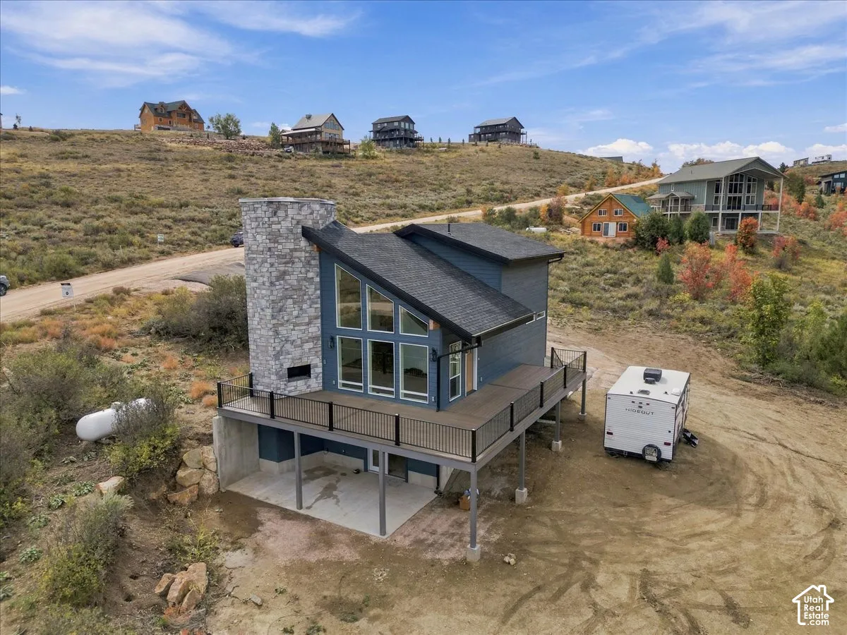 Contemporary architectural design featuring a prominent stone-clad chimney, expansive window wall, and a spacious elevated deck with dark railings