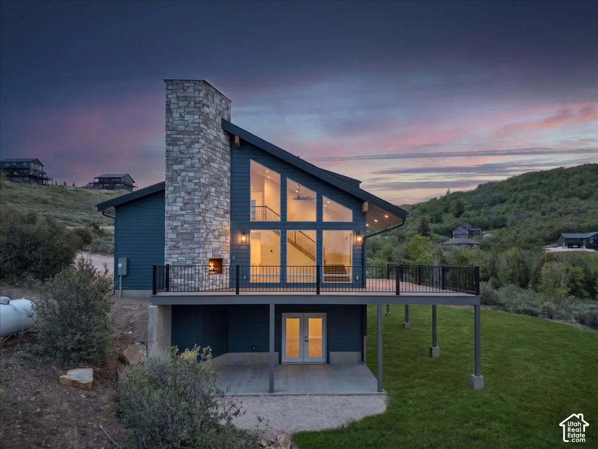 Modern architectural design with expansive windows, a large stone chimney, and a raised deck with dark railings