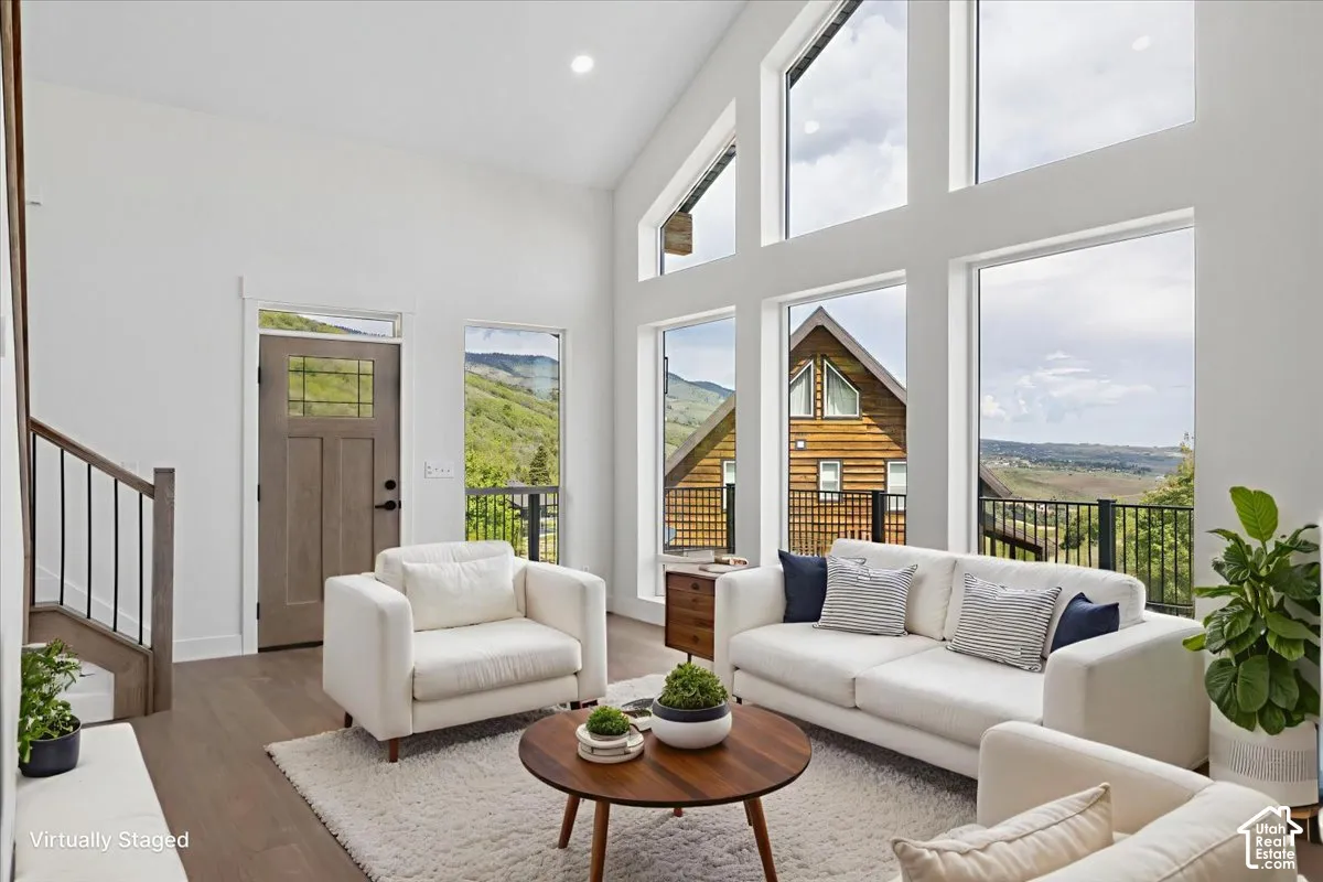 Vaulted ceilings with expansive floor-to-ceiling windows, wood-finish flooring, and a modern staircase with dark metal railings