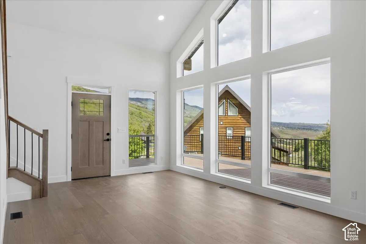 Vaulted ceiling with recessed lighting, expansive floor-to-ceiling windows, wood-finish flooring, and a wood-panel entry door with transom window