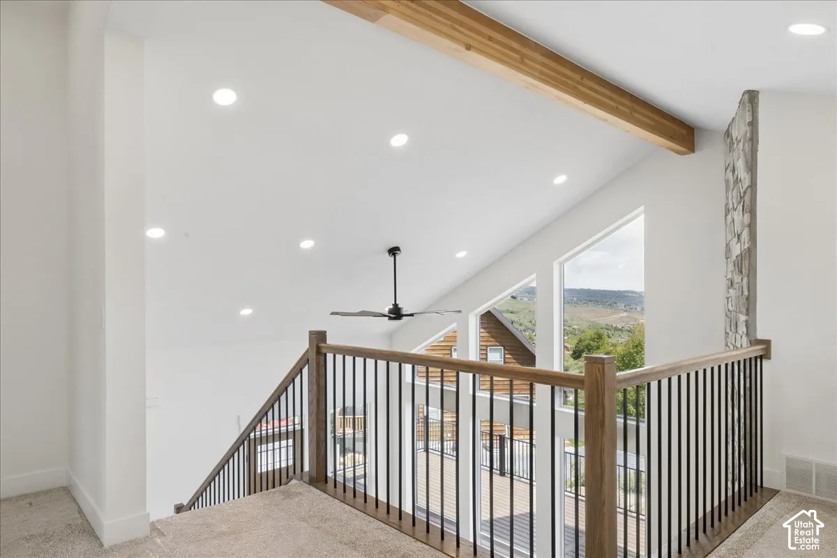 Vaulted ceiling with exposed wood beam, recessed lighting, stone accent wall, and a black ceiling fan