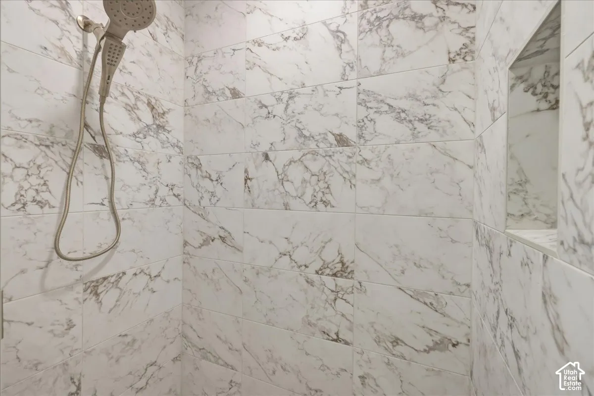 Walk-in shower with white and gold veined tile, a recessed niche, and a brushed gold handheld showerhead
