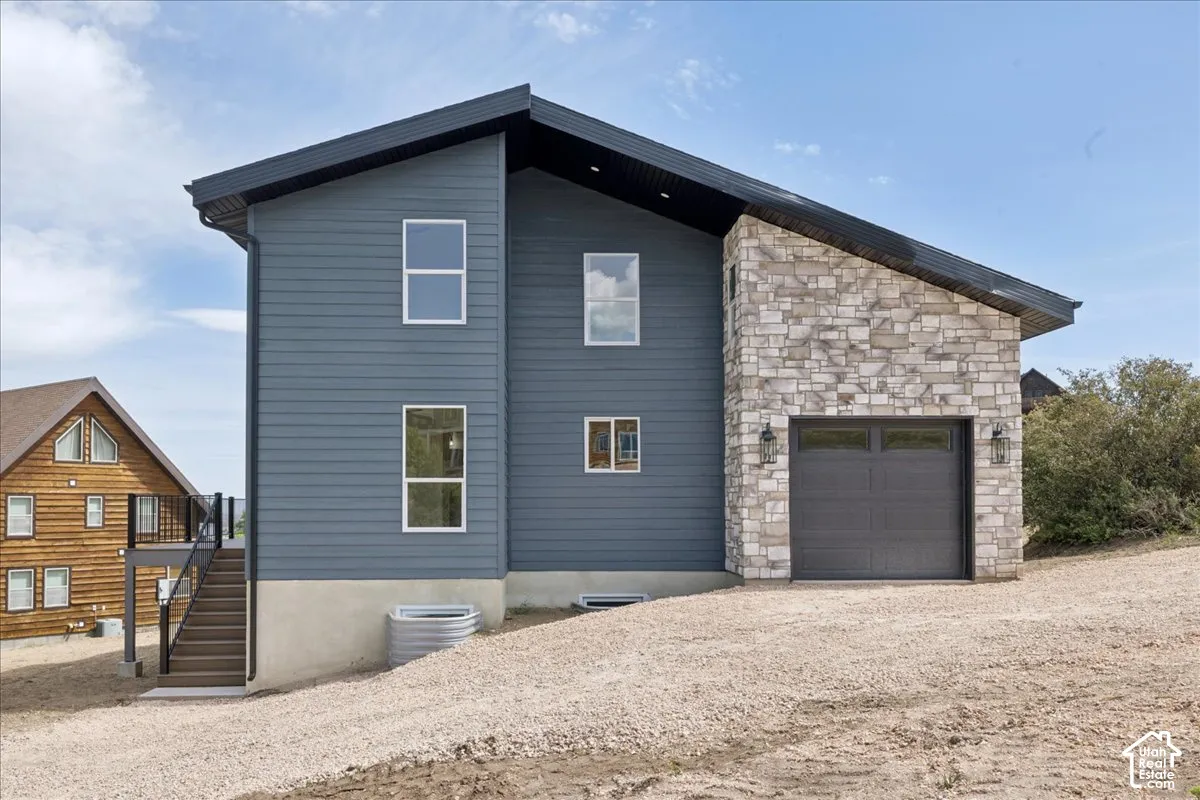 Modern exterior with a slanted roofline, blue siding, stone accent wall, and an attached garage with exterior sconce lighting