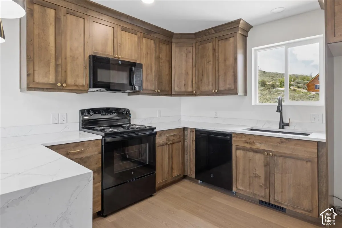 Kitchen with wood-finish cabinetry, white countertops, stainless steel sink with matte black faucet, black appliances, and wood-finish flooring