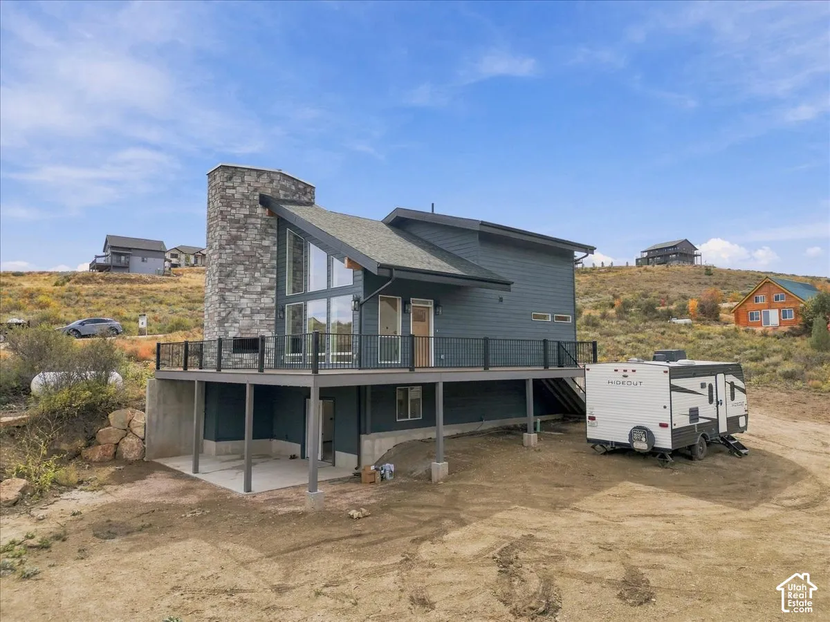 Modern architectural design featuring an angular roofline, stone-clad chimney, expansive windows, a spacious deck with metal railings, and a walk-out lower level