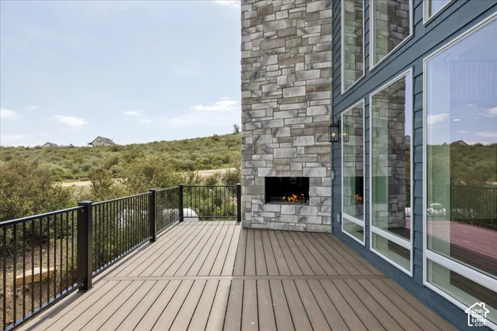 Expansive outdoor deck featuring wood-finish flooring, black metal railings, and a built-in stone-clad outdoor fireplace