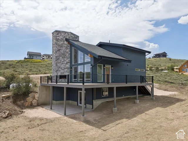 Sleek contemporary exterior featuring a stone-clad chimney, expansive deck with black railings, and a lower-level patio