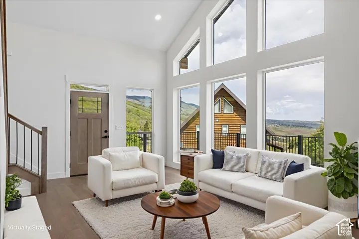Vaulted ceilings with expansive floor-to-ceiling windows, wood-finish flooring, and a modern staircase with dark metal railings