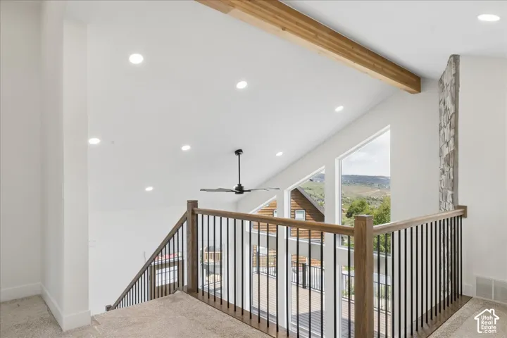 Vaulted ceiling with exposed wood beam, recessed lighting, stone accent wall, and a black ceiling fan