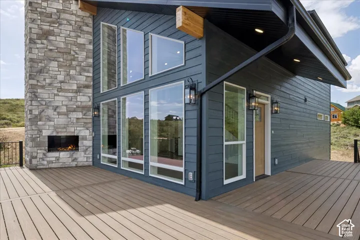 Expansive composite deck featuring a built-in outdoor fireplace with stone surround, large multi-pane windows, and modern exterior lighting