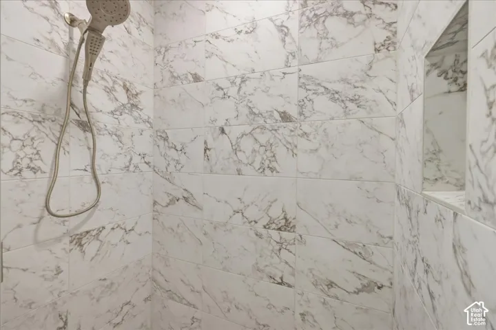 Walk-in shower with white and gold veined tile, a recessed niche, and a brushed gold handheld showerhead