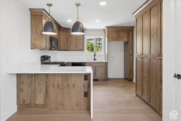 Kitchen featuring wood-finish cabinetry, white countertops, a black range, and two pendant light fixtures