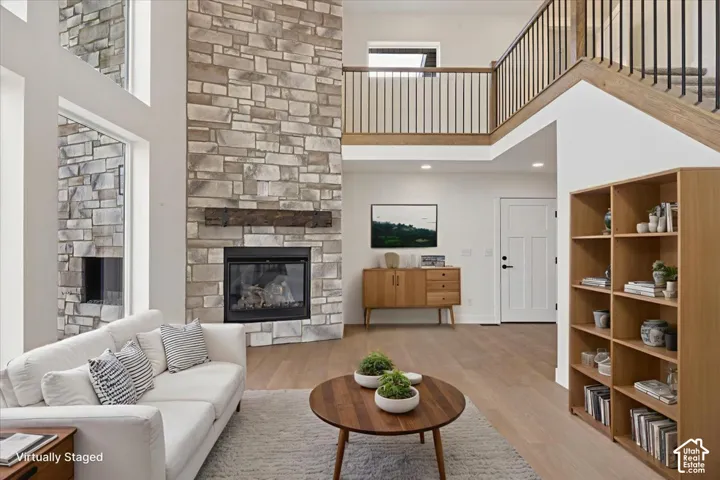 Two-story stone fireplace with a dark wood mantel, wood-finish flooring, two-story windows, and a wood staircase with black balusters