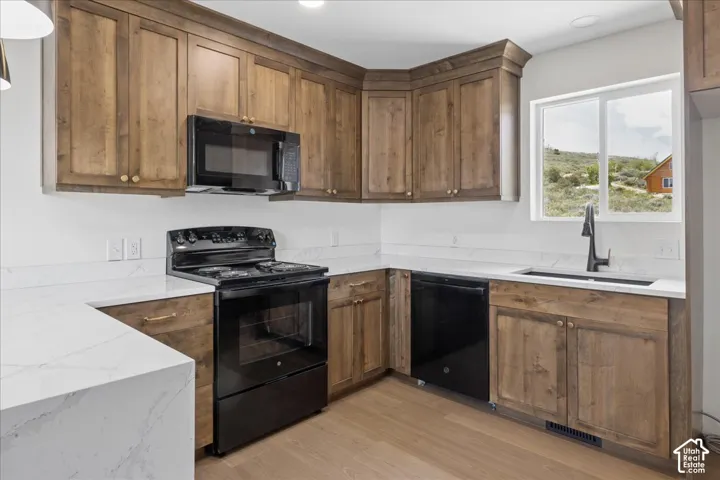 Kitchen with wood-finish cabinetry, white countertops, stainless steel sink with matte black faucet, black appliances, and wood-finish flooring
