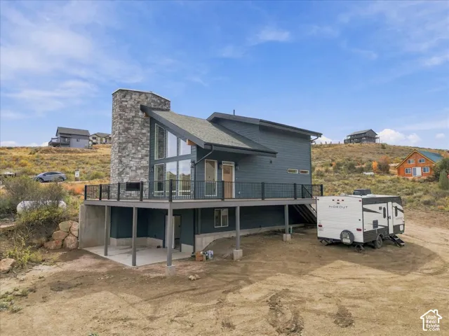 Modern architectural design featuring an angular roofline, stone-clad chimney, expansive windows, a spacious deck with metal railings, and a walk-out lower level
