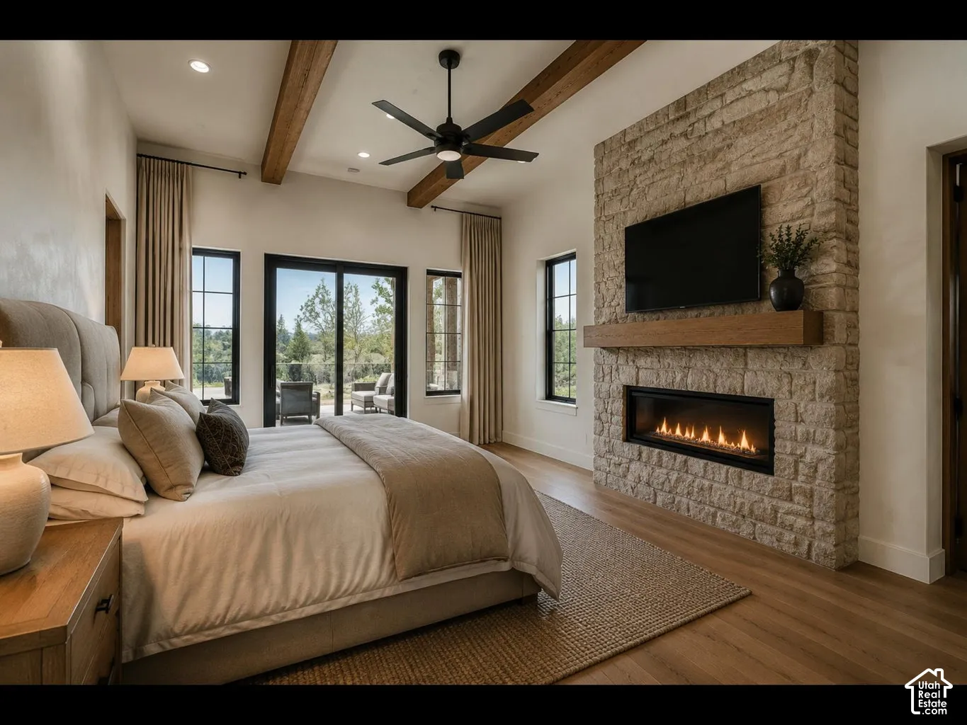 Vaulted ceiling with exposed wood beams and recessed lighting, stone fireplace with a wood mantel and linear insert, wood-finish flooring, black frame sliding glass door, and black frame windows