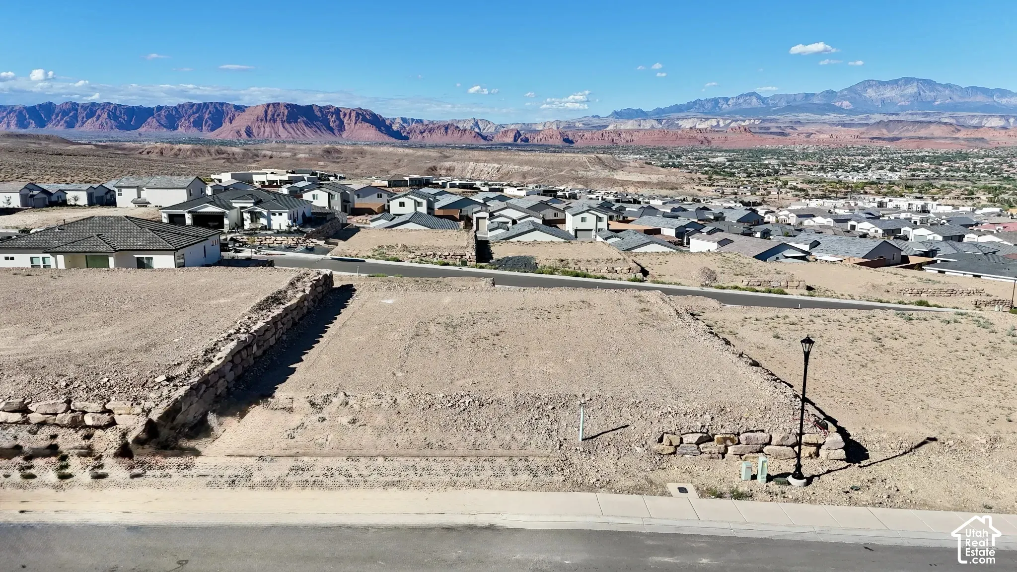 Graded building lot featuring a retaining wall, a paved street, and a community street lamp