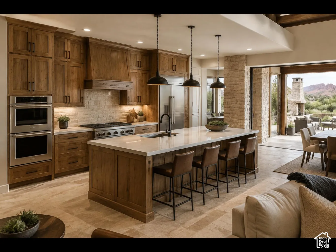Gourmet kitchen with wood-finish cabinetry, stainless steel double ovens, a large center island with seating, and stone flooring
