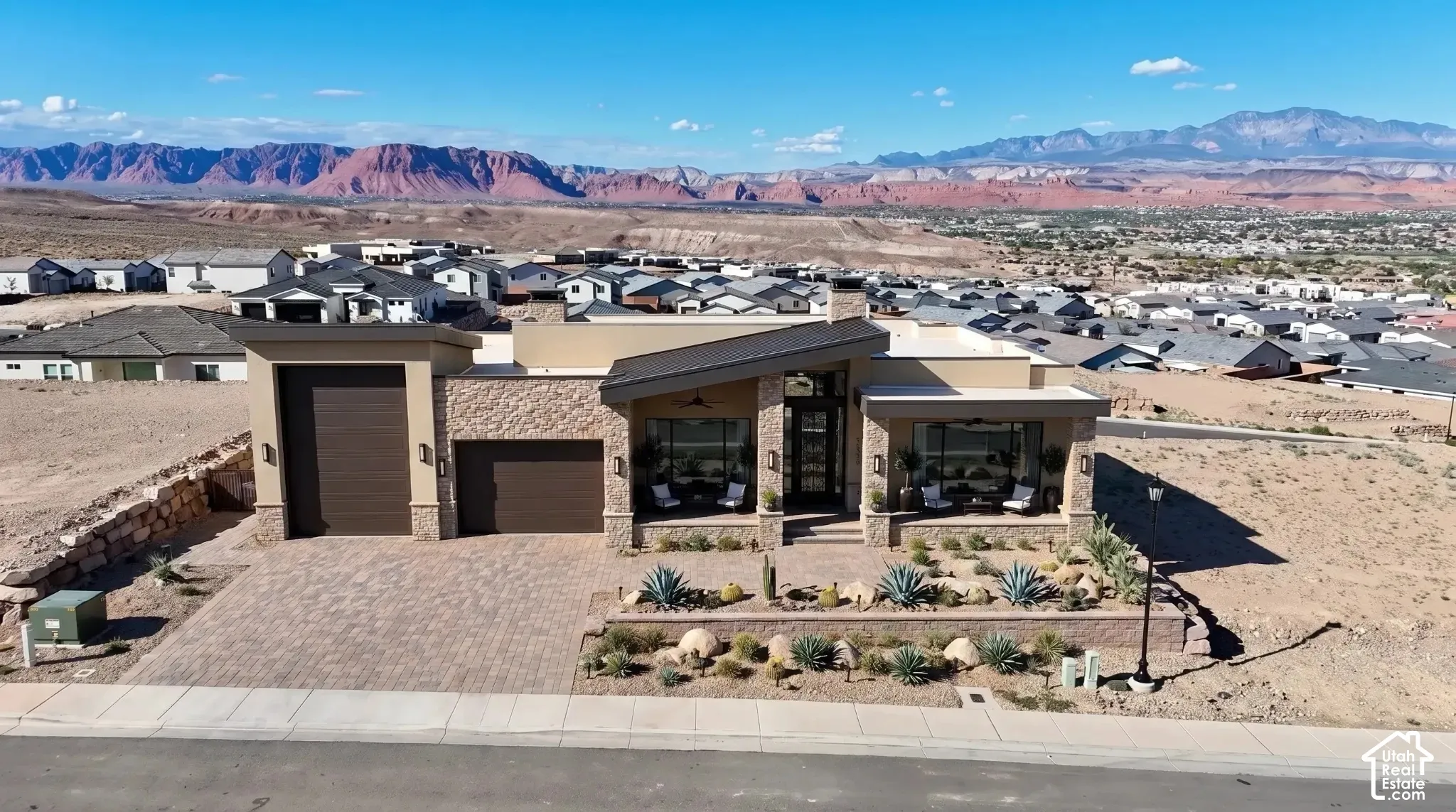 Contemporary desert architecture featuring a stone and stucco exterior, a paver driveway, and a covered front entry