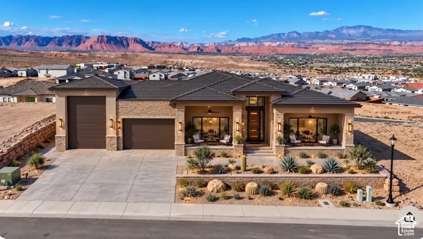 Stucco and stone exterior with a tile roof, dual garage doors, and a desert-inspired landscaped front yard with a retaining wall
