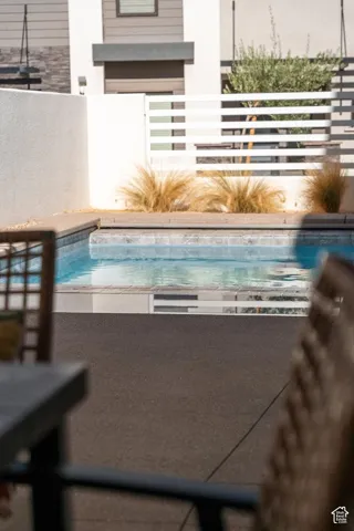 Swimming pool with stone coping, surrounded by decorative grasses and a white slatted fence