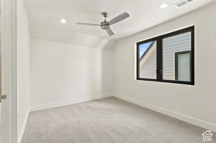 Neutral carpet flooring, white walls, black-framed window, recessed lighting, and a ceiling fan