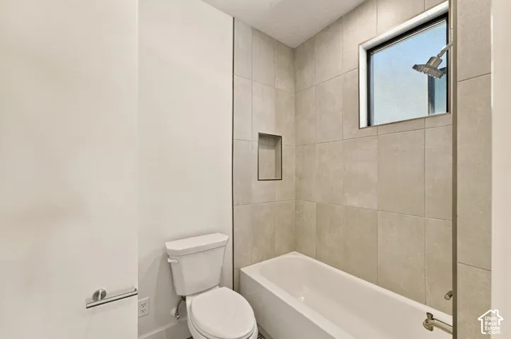 White bathtub with polished chrome fixtures, integrated wall niche, and large format tiled walls