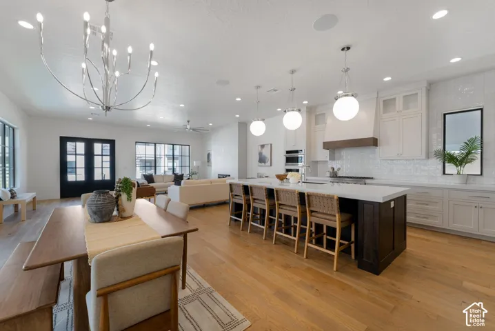 Open-concept living space featuring wood-finish flooring, a large kitchen island with pendant lighting, white cabinetry, and stainless steel built-in appliances
