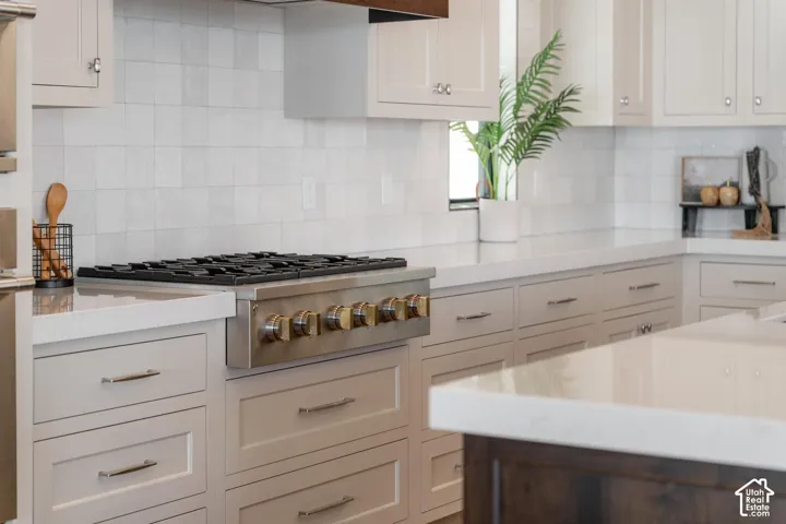 Built-in stainless steel range, light-toned cabinetry, solid surface countertops, square tile backsplash, and an integrated kitchen island