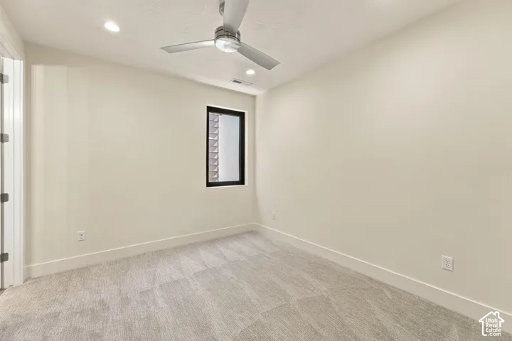 Recessed lighting, ceiling fan, neutral wall paint, single window with black frame, and gray patterned carpeting