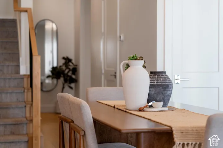 Wood-finish dining table with upholstered chairs, staircase with carpeted treads and wood handrail, and a paneled interior door