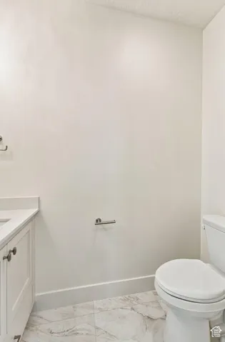 White shaker-style vanity with a light-toned countertop, white toilet, and marble-look floor tiling