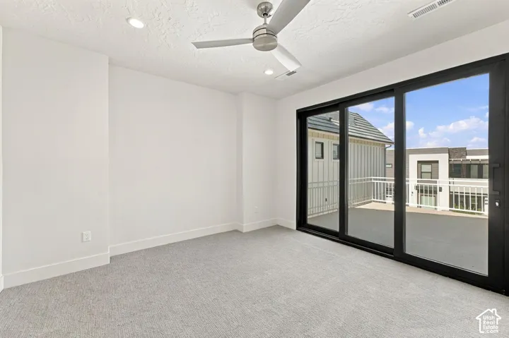 Expansive sliding glass door leading to an outdoor balcony, featuring a modern ceiling fan, recessed lighting, and light-colored carpeting