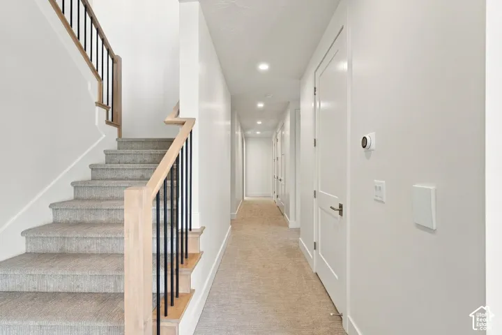 Staircase with light wood handrails, black metal balusters, and carpeted treads