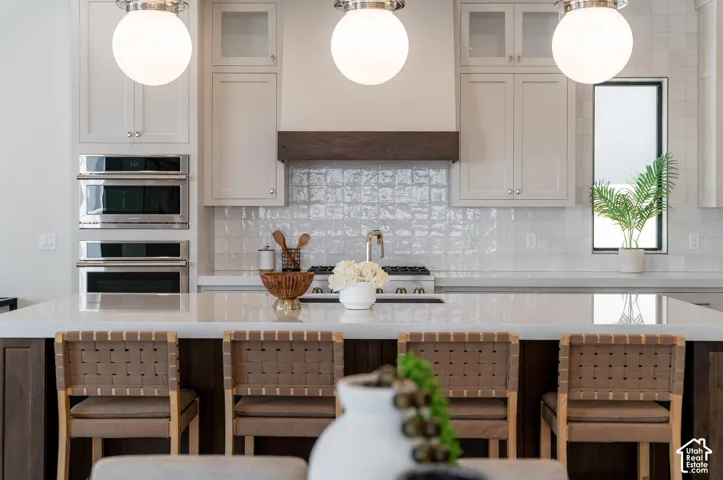 Kitchen featuring a white quartz-finish island, white subway tile backsplash, stainless steel double wall ovens, and custom cabinetry with glass-front accents