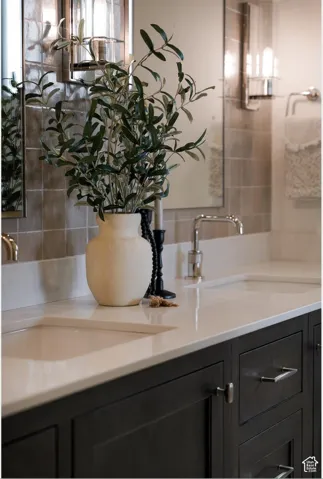 Dual undermount sinks, polished chrome faucets, dark wood-finish cabinetry, light-toned countertops, and wall-mounted light fixtures