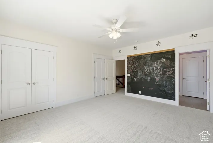 Plush carpet flooring, white walls, multiple panel doors, and a ceiling fan with light fixture