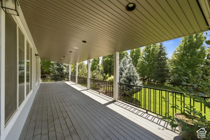 Expansive covered deck featuring composite decking, recessed lighting, white columns, and black metal railings overlooking mature trees and green space