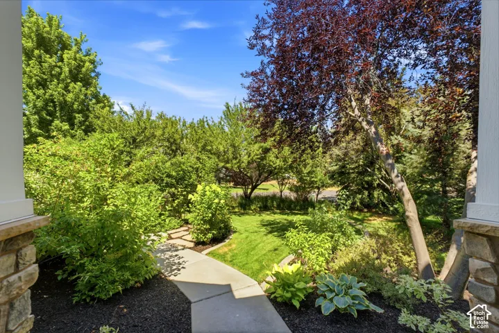 Concrete pathway featuring a manicured lawn, mature trees, and diverse landscaping with mulch beds
