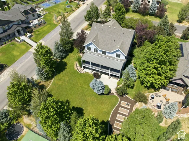 Two-story residence with a covered porch, expansive green lawn, mature trees, and a paved patio area