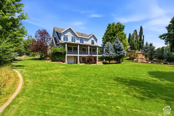Expansive green lawn with a defined pathway, a light blue siding exterior, a multi-level deck, and mature landscaping