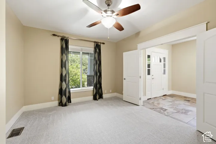 Spacious room featuring light-colored carpeting, a ceiling fan with wood-finish blades, and a large window