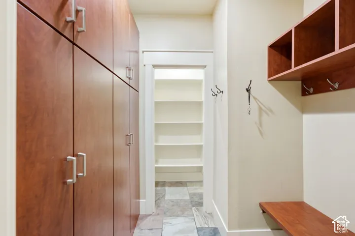 Wood-finish cabinetry with silver-tone hardware, built-in shelving, wood-finish storage bench, and ceramic tile flooring