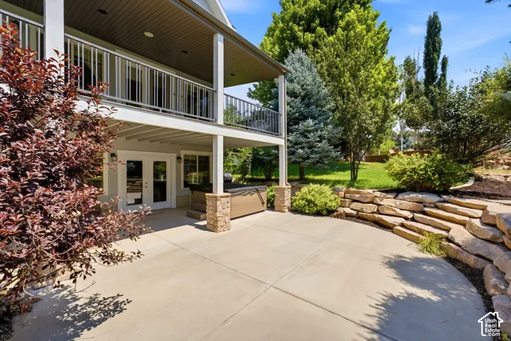 Expansive concrete patio with a stone retaining wall, covered balcony, and double glass-paneled doors