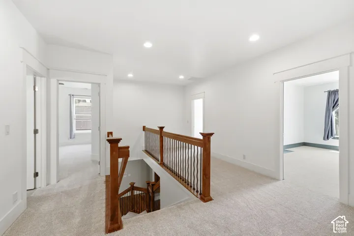 Carpeted landing featuring a wood staircase with metal balusters, recessed lighting, and white trim