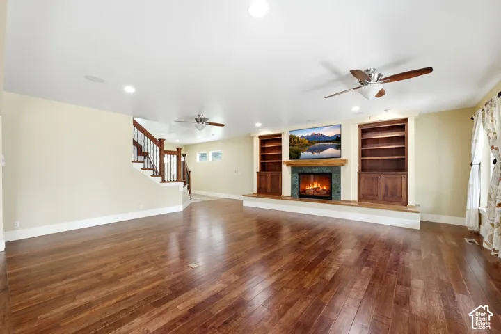 Hardwood flooring, recessed lighting, built-in shelving, a fireplace with a stone surround, and a staircase with wood banisters