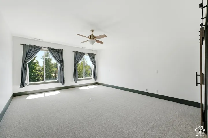 Primary Bathroom. Spacious room featuring light gray carpeting, a ceiling fan, and two large windows