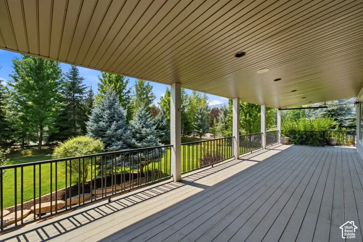 Expansive covered deck with composite decking, recessed lighting, white support columns, and black metal railings overlooking mature trees and landscaped grounds