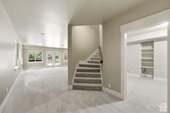 Expansive carpeted room with multiple windows, glass French doors, and recessed lighting